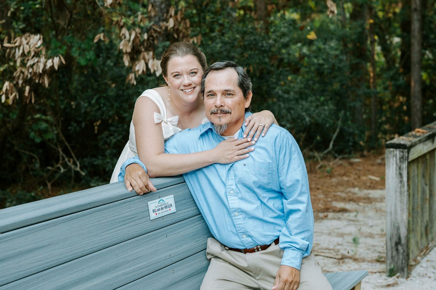 A couple in light blue and white outfits share tender moments while sitting on wooden steps outdoors.