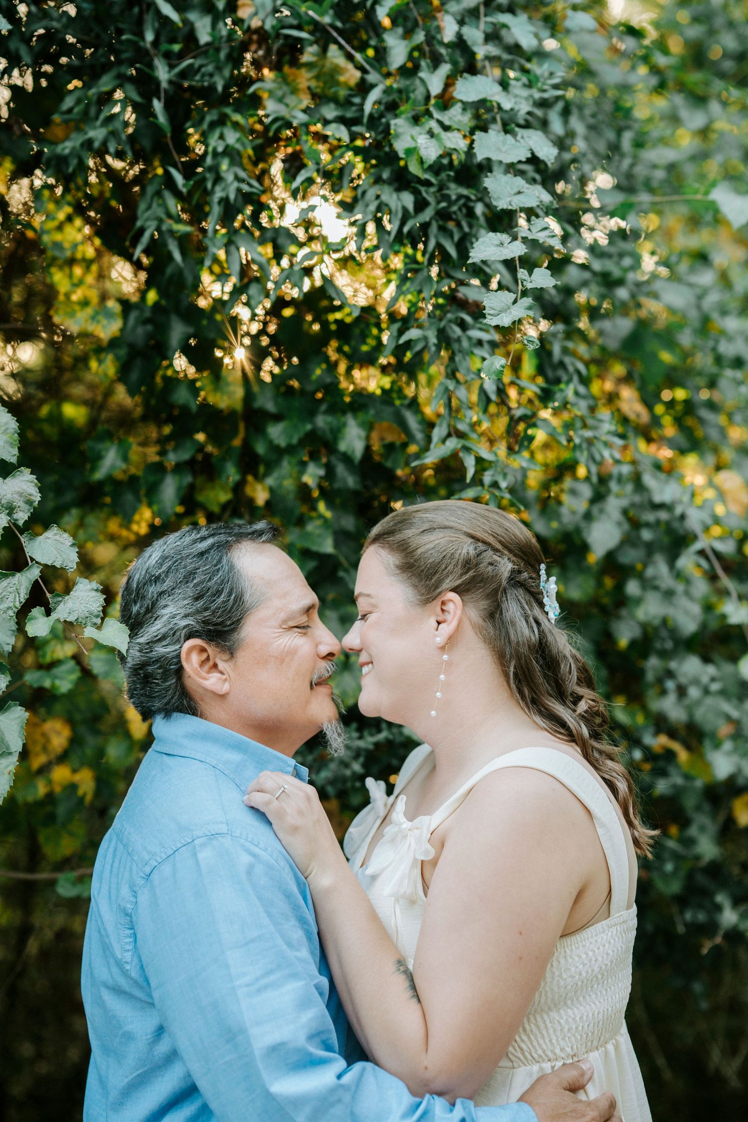 A romantic couple shares an intimate moment under blooming trees with yellow flowers.
