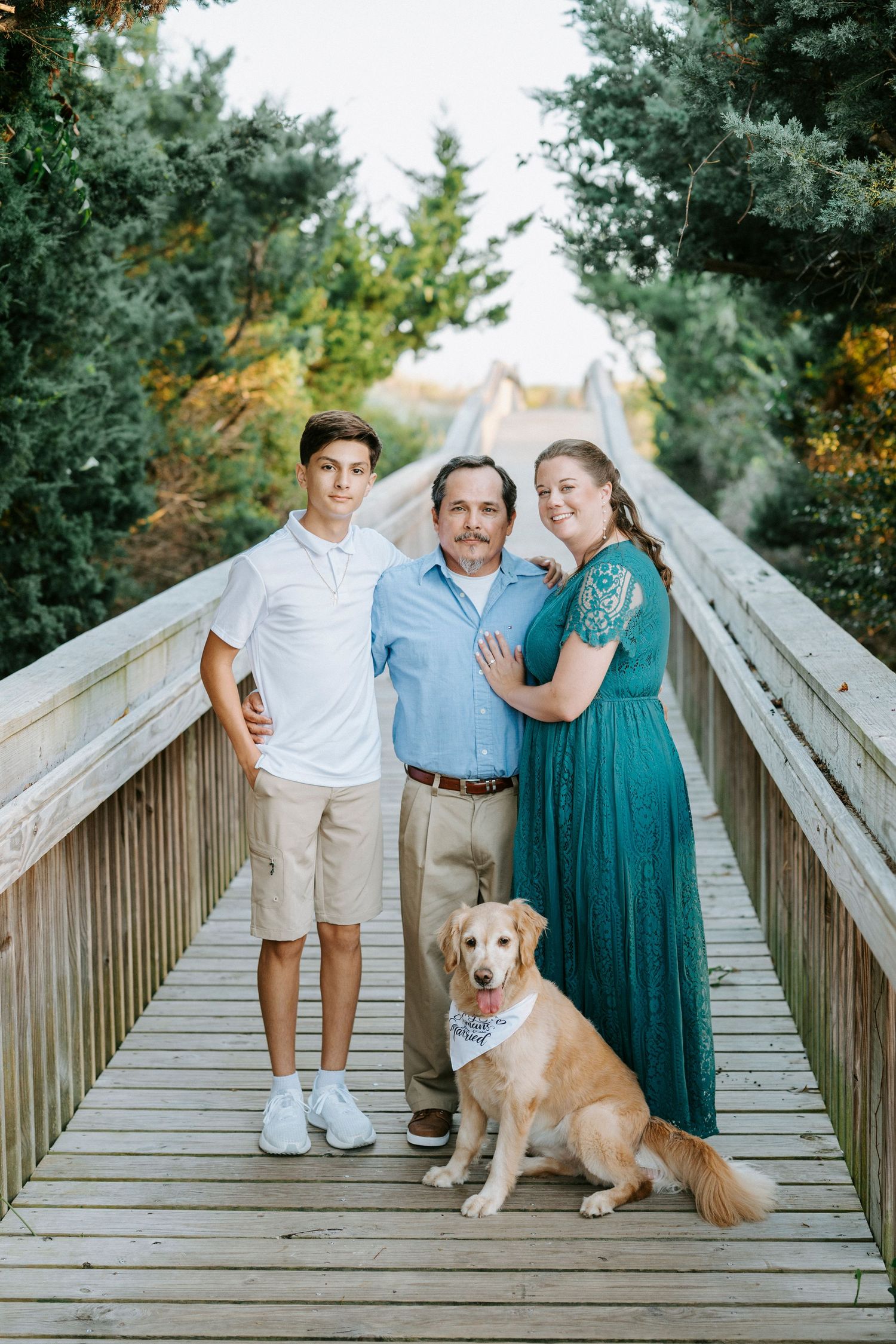 A family and their golden retriever pose together on a wooden boardwalk surrounded by greenery.