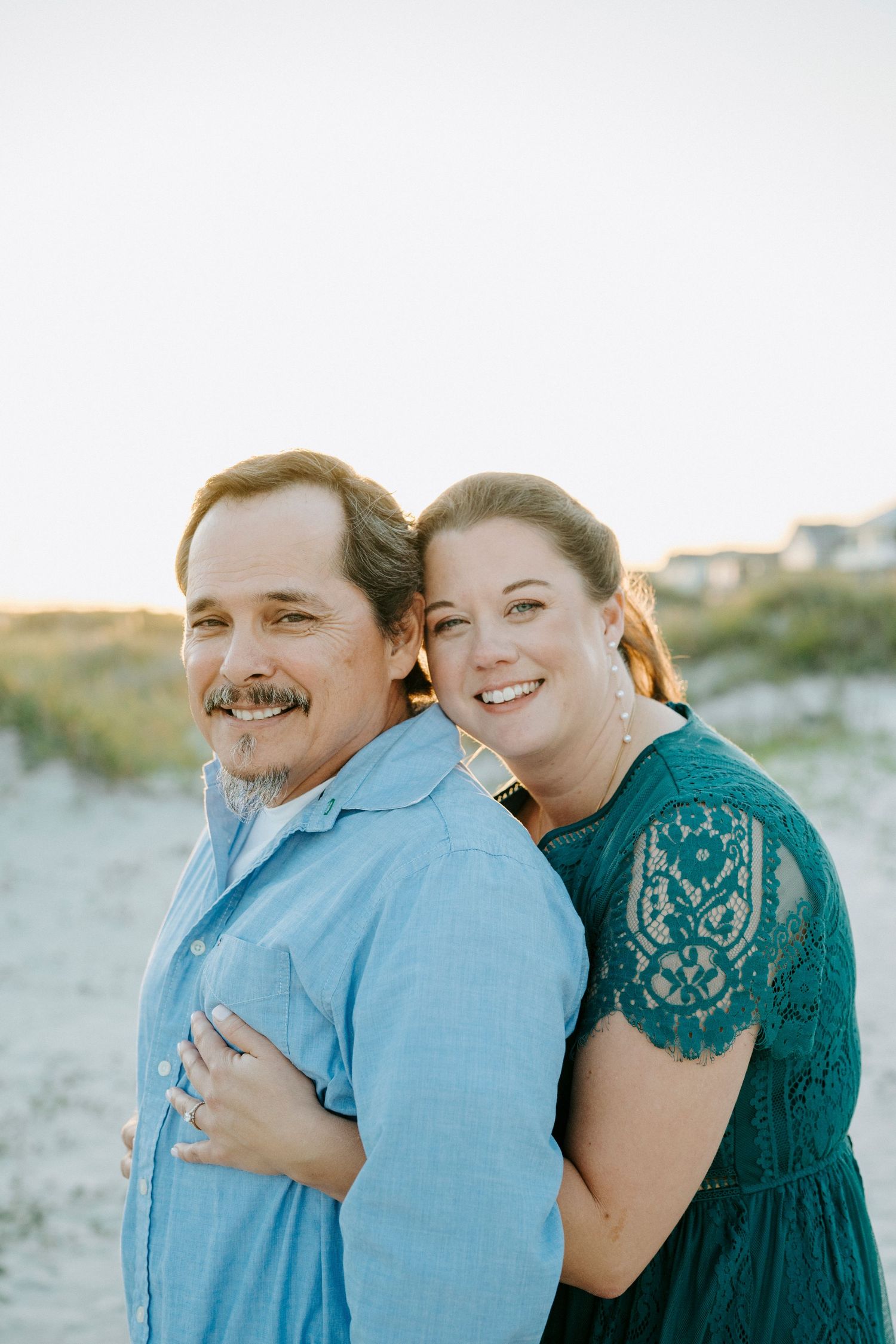 A couple in blue and teal outfits share intimate moments during a beach photoshoot.