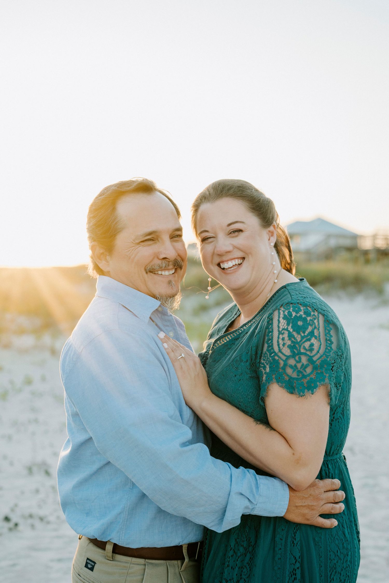 A couple shares joyful moments together on a beach during golden hour, wearing blue and green attire.