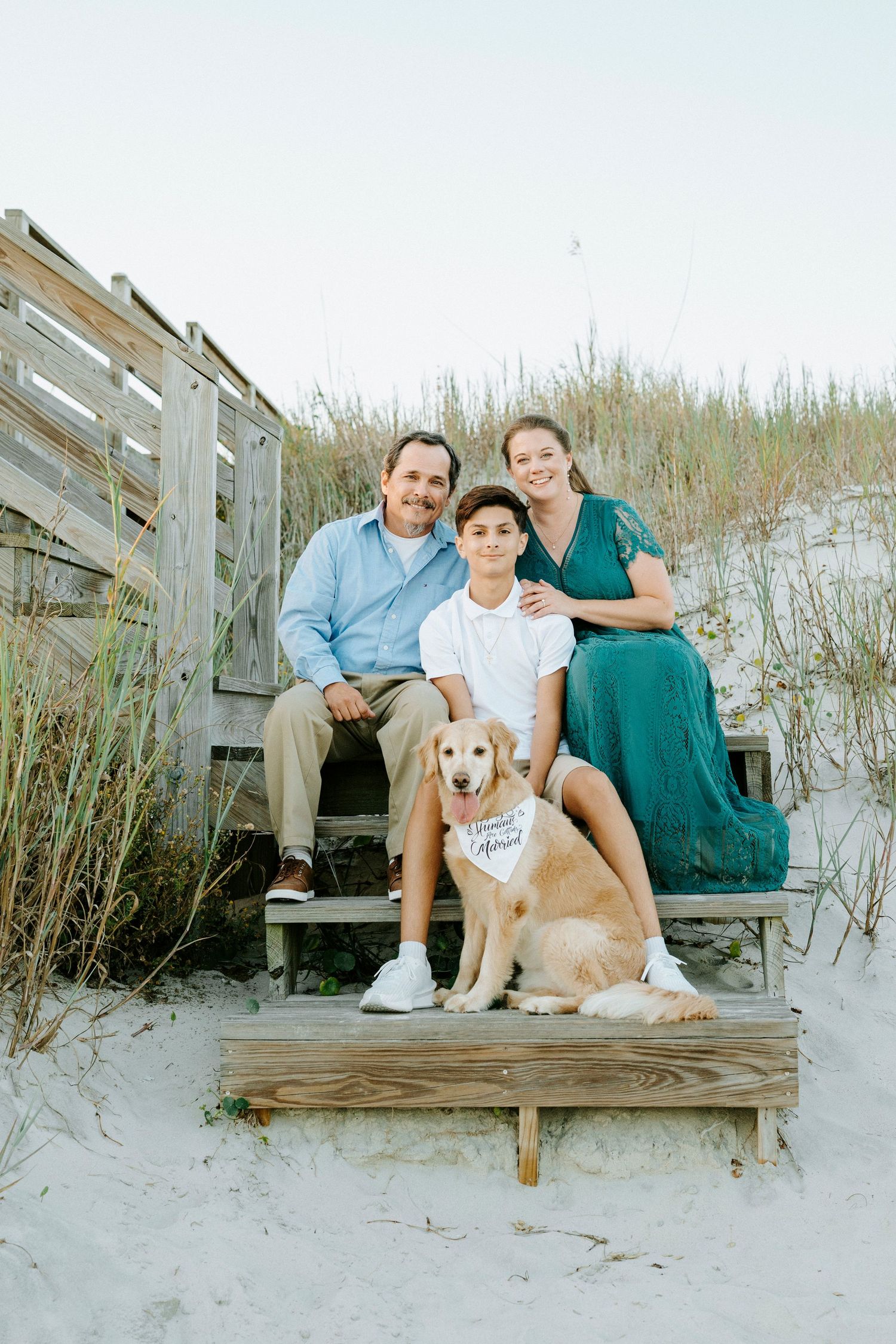 Family sitting on wooden boardwalk at beach with their golden retriever dog.
