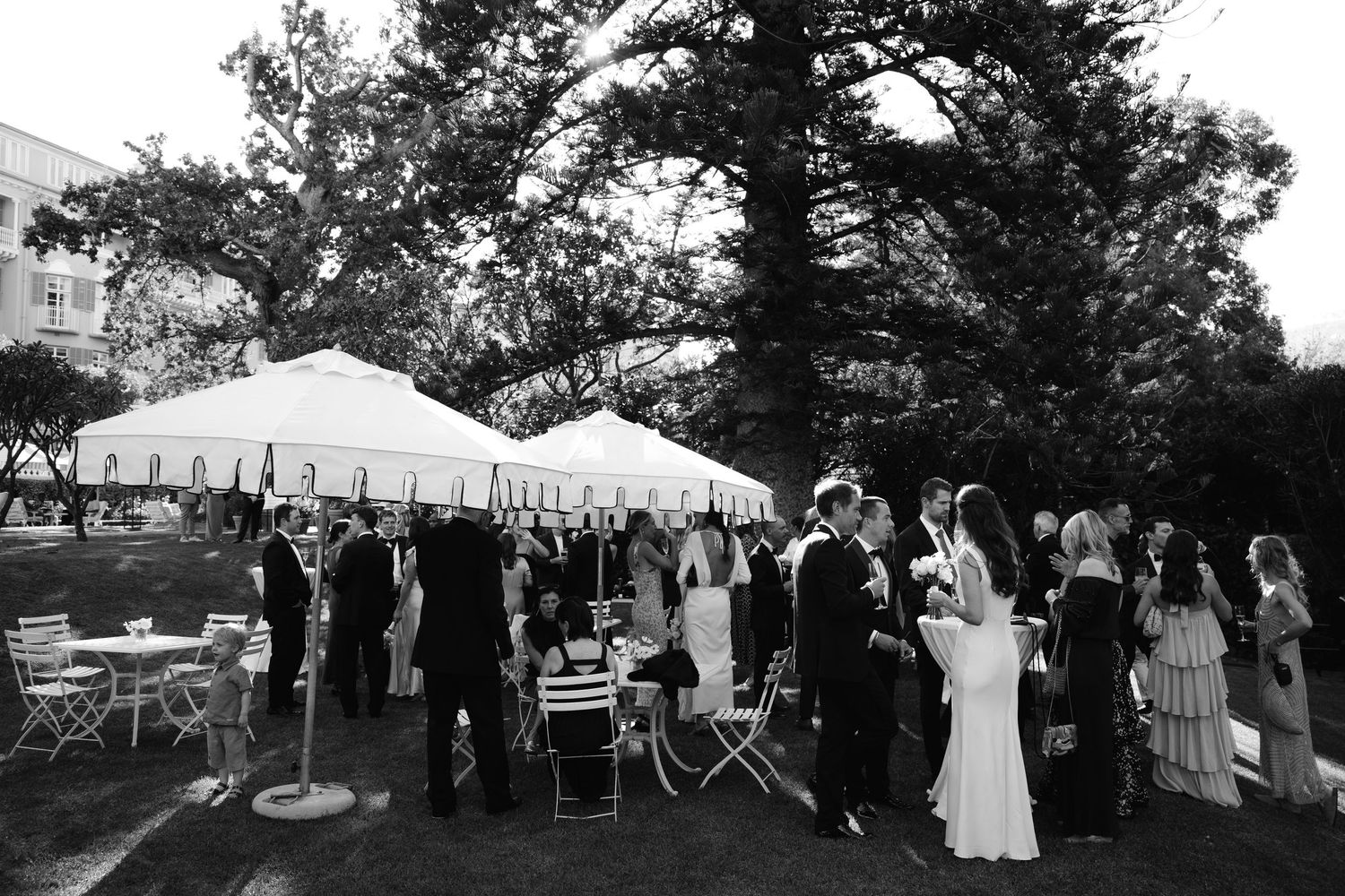 A series of black and white wedding photos showing guests mingling at an outdoor reception under trees and tents.
