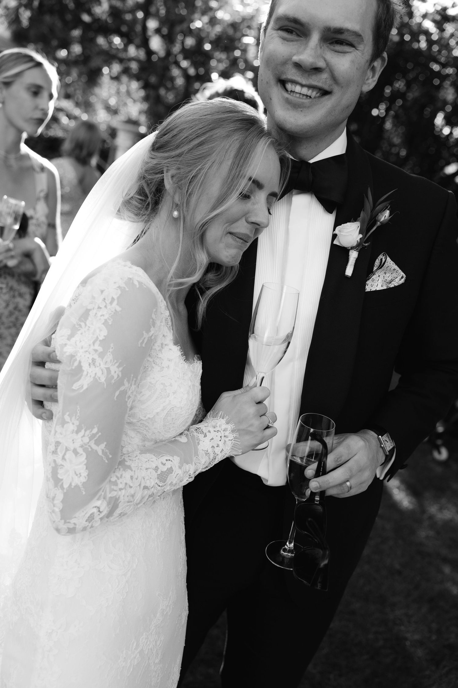 A tender black and white wedding moment captured outdoors with the bride in lace and groom in classic tuxedo.