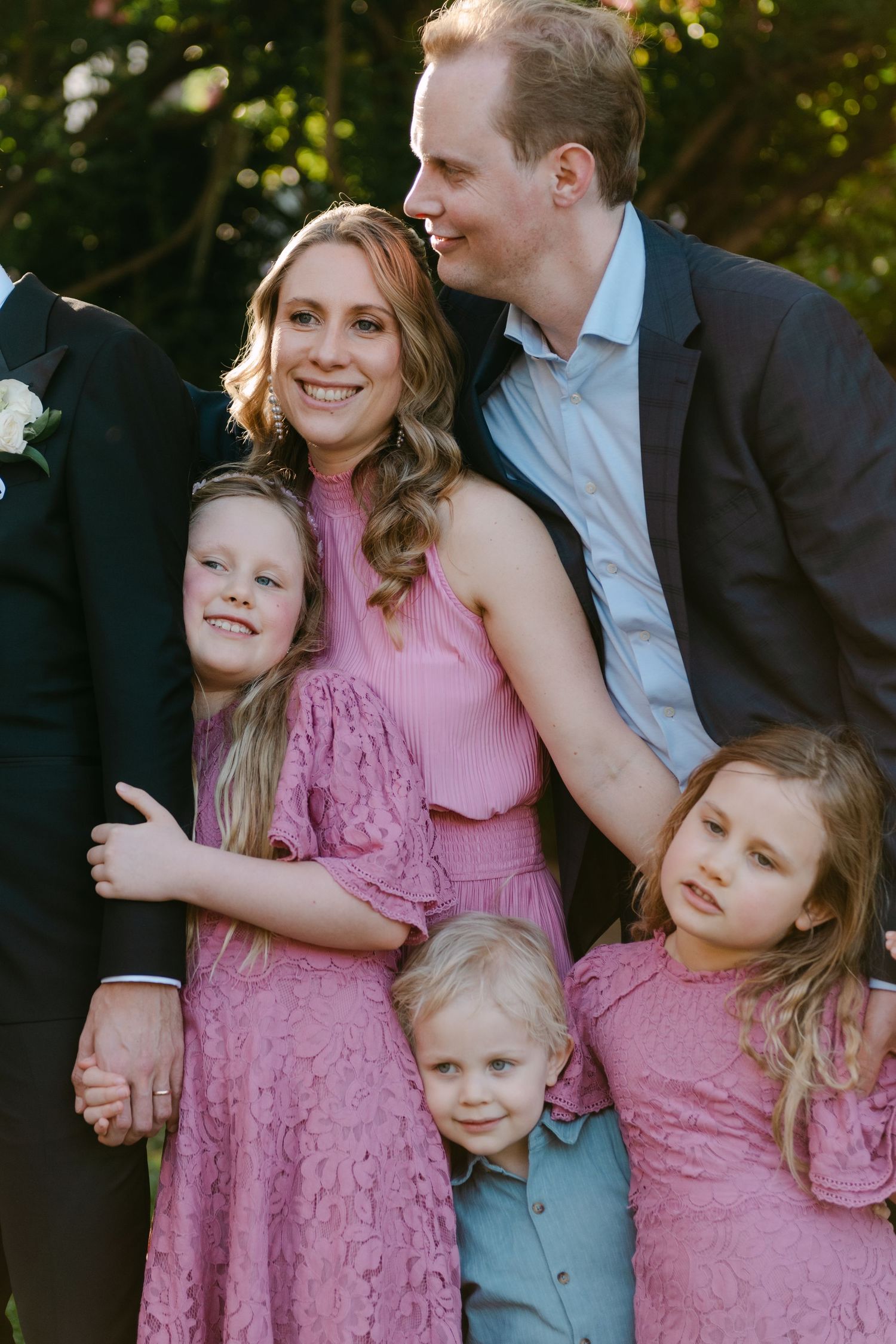 Family wearing pink and blue outfits poses together outdoors in a candid moment during a photo session.
