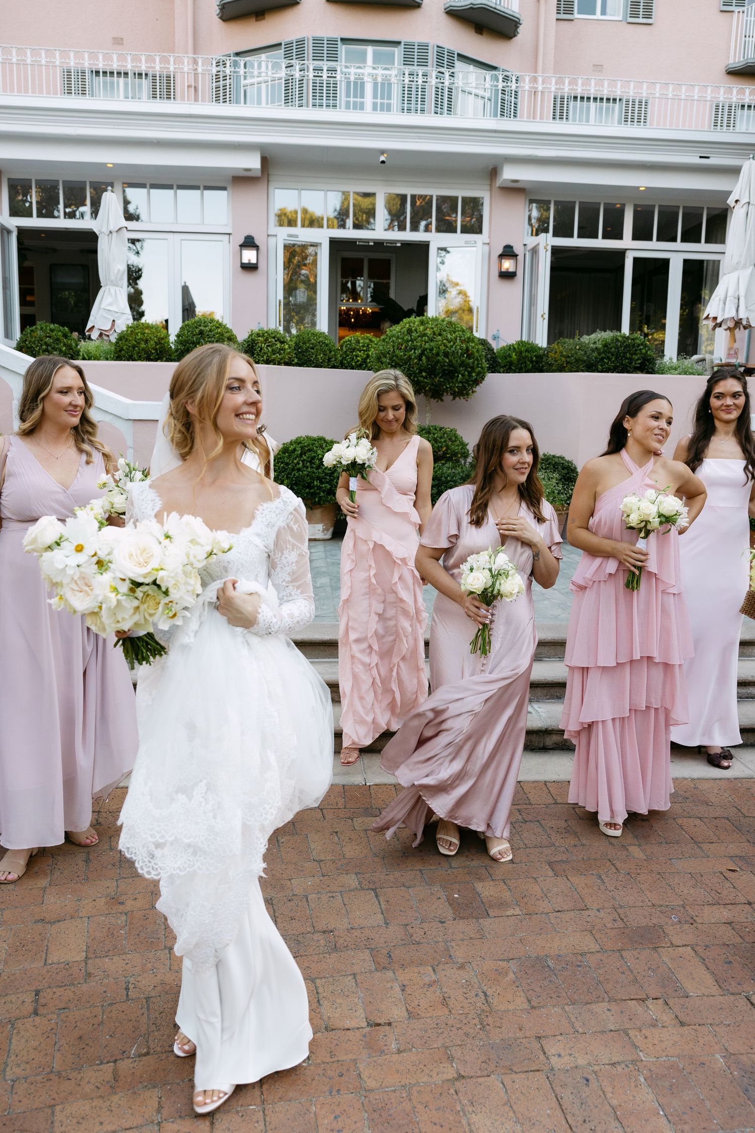 Wedding party in pink and white dresses celebrating on brick patio of luxury hotel.