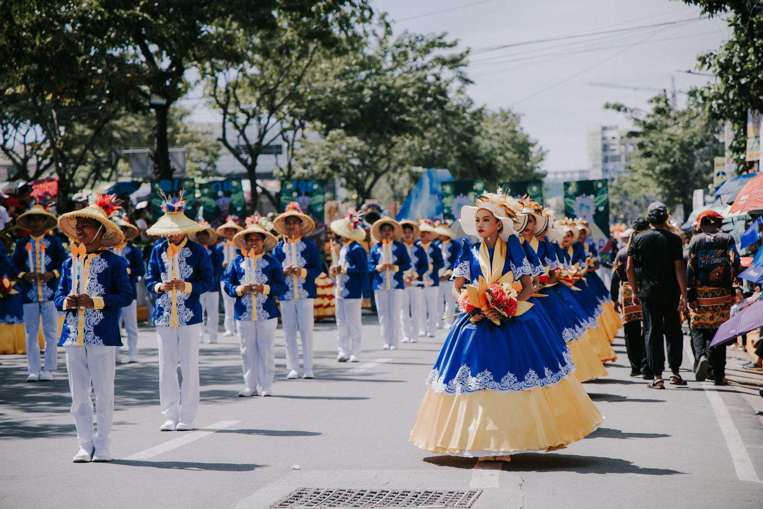 Marching band members in white uniforms performing on a sunny street.