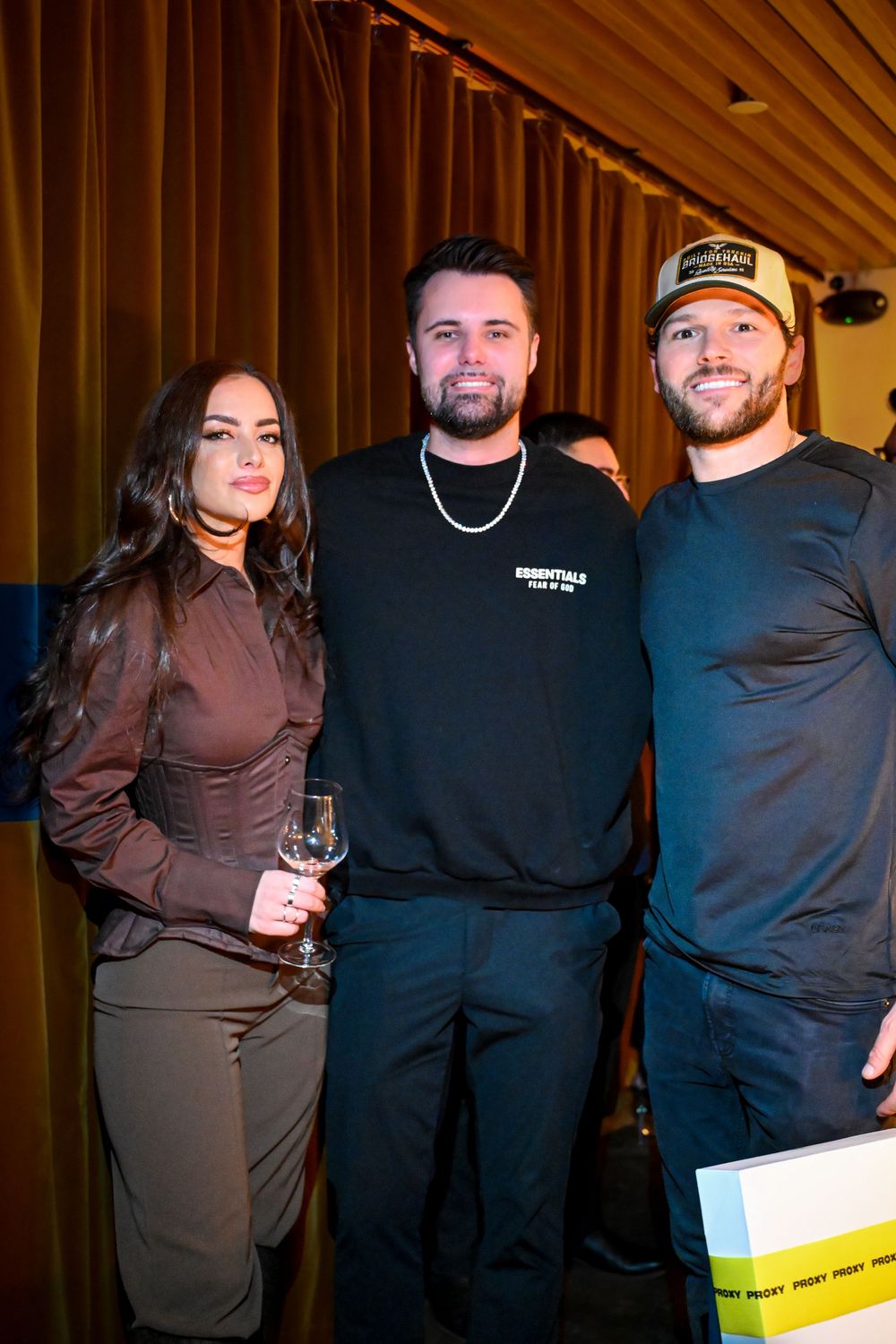A group of people wearing black and brown clothing pose together at what appears to be a social gathering.