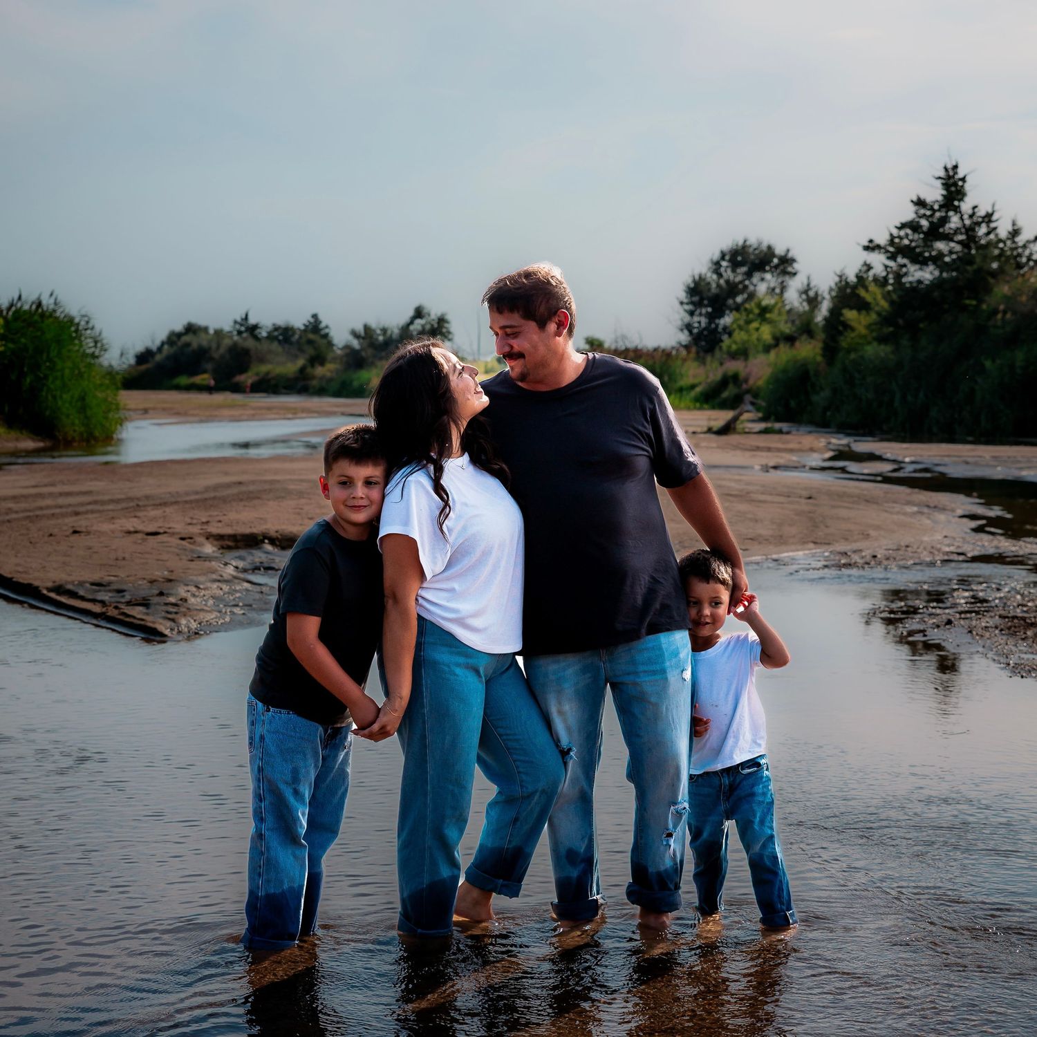 A family wearing matching denim stands in shallow water at the beach during sunset, creating a playful moment together.