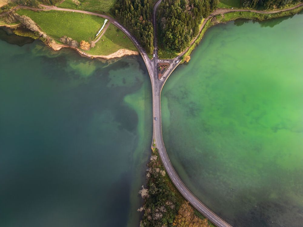 Aerial panoramic view of a long bridge stretching across emerald green waters with lush coastline visible.
