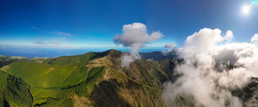 Stunning panoramic mountain landscape with rolling green hills and dramatic clouds against vibrant blue skies.