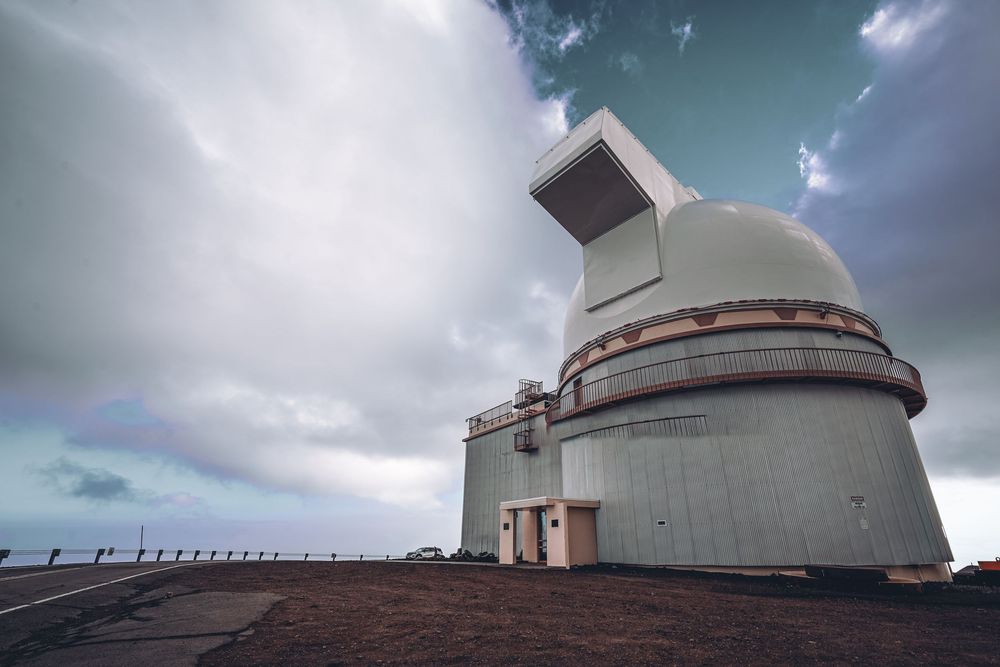 Panoramic view of white observatory domes under dramatic cloudy skies at a mountaintop research facility.