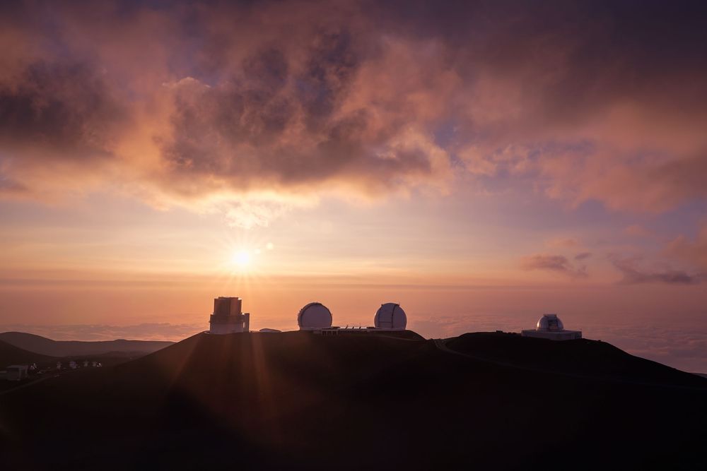 A dramatic sunset casts golden light over silhouetted mountains and clouds in a panoramic landscape view.