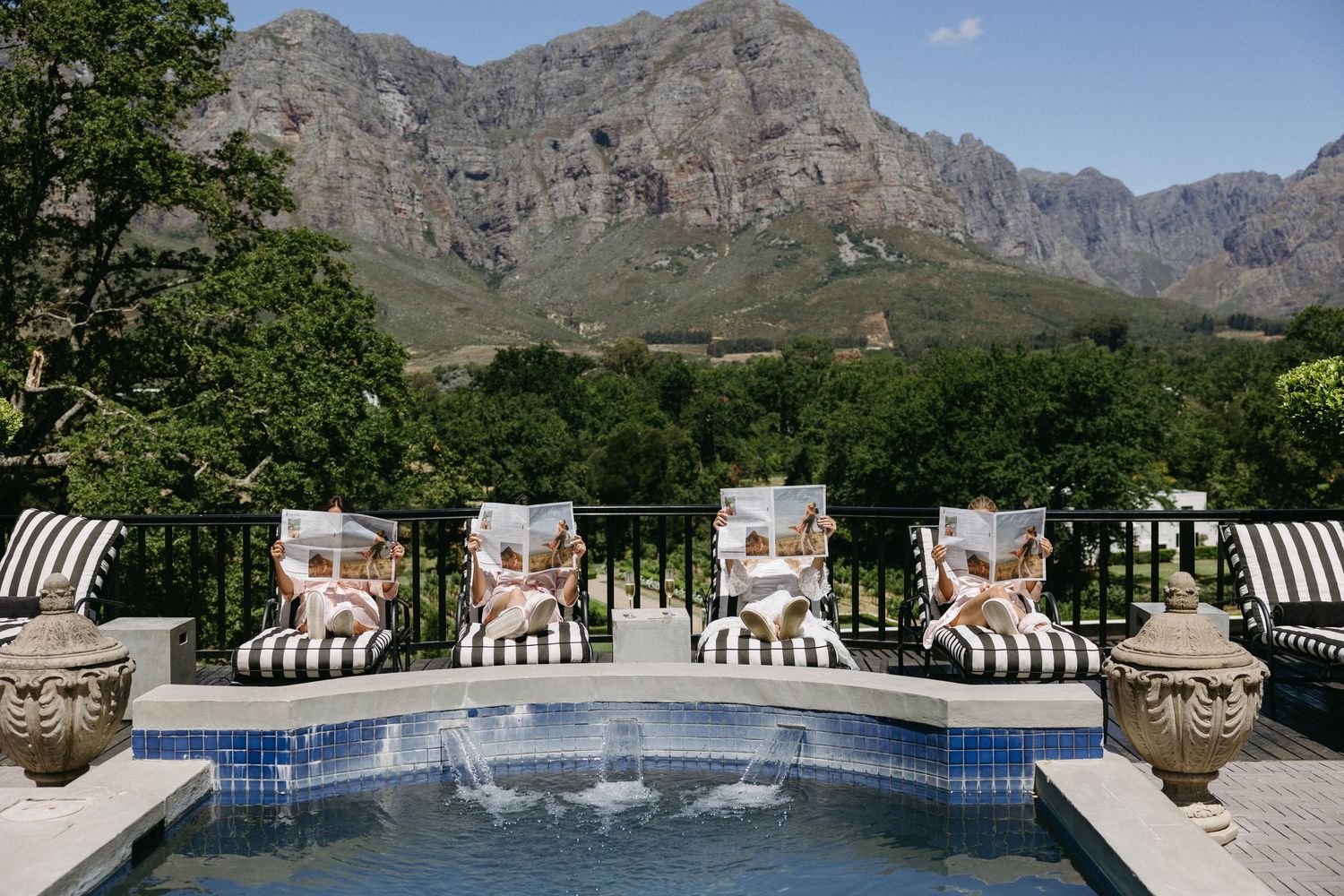A panoramic view of a luxurious swimming pool surrounded by lounge chairs with dramatic mountain peaks in the background.
