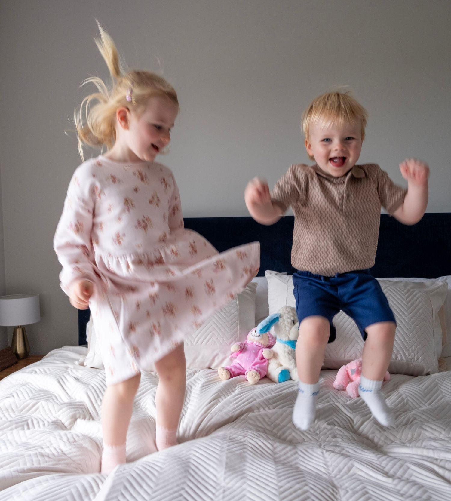 Two children in casual clothing jumping and playing together on a white bed in a series of action shots.