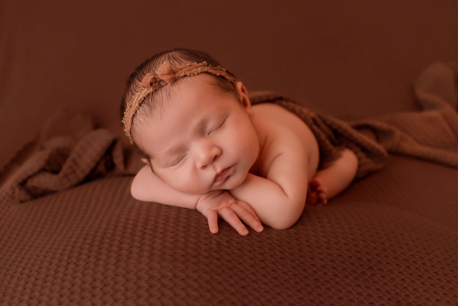 Newborn sleeping peacefully in frog pose on brown textured backdrop.