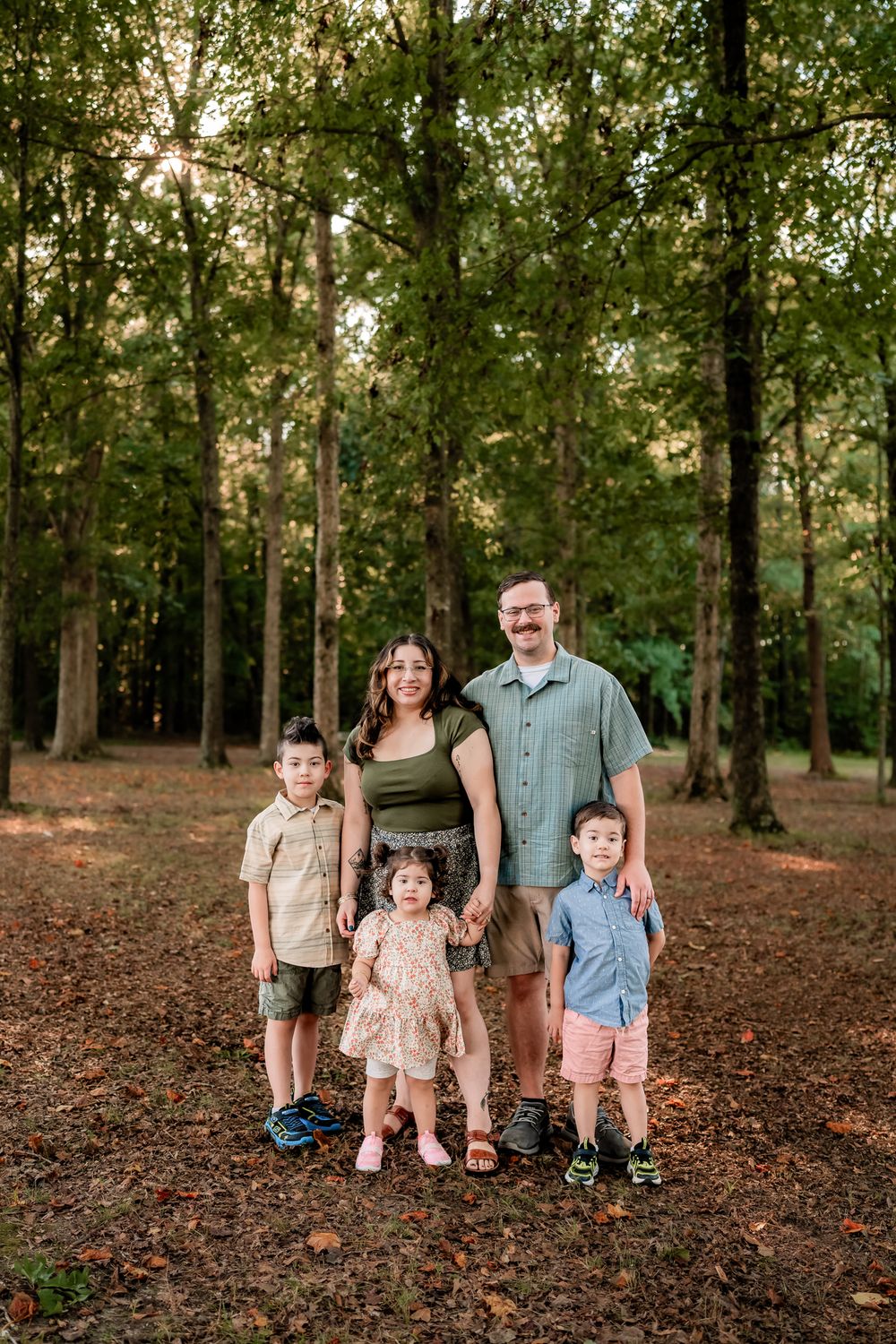A family stands together on fallen autumn leaves in a wooded area during an outdoor photo session.