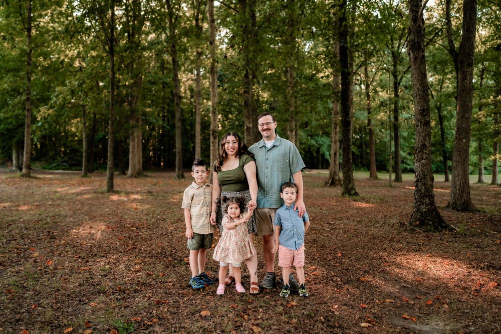 A group of people walking together through a wooded area with sunlight filtering through the trees.