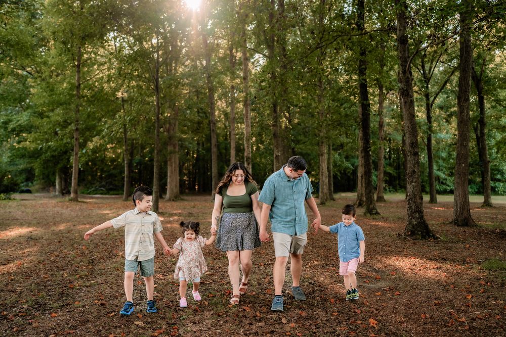 A family walks together holding hands along a sunlit forest path on an autumn afternoon.