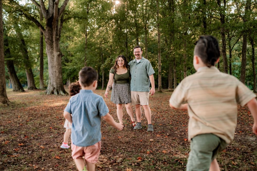 A family walks together holding hands through a wooded park trail on an autumn afternoon.