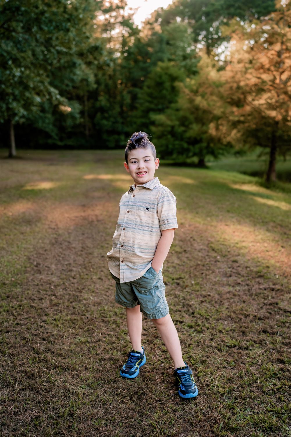 A child stands playfully in a grassy field during golden hour lighting.