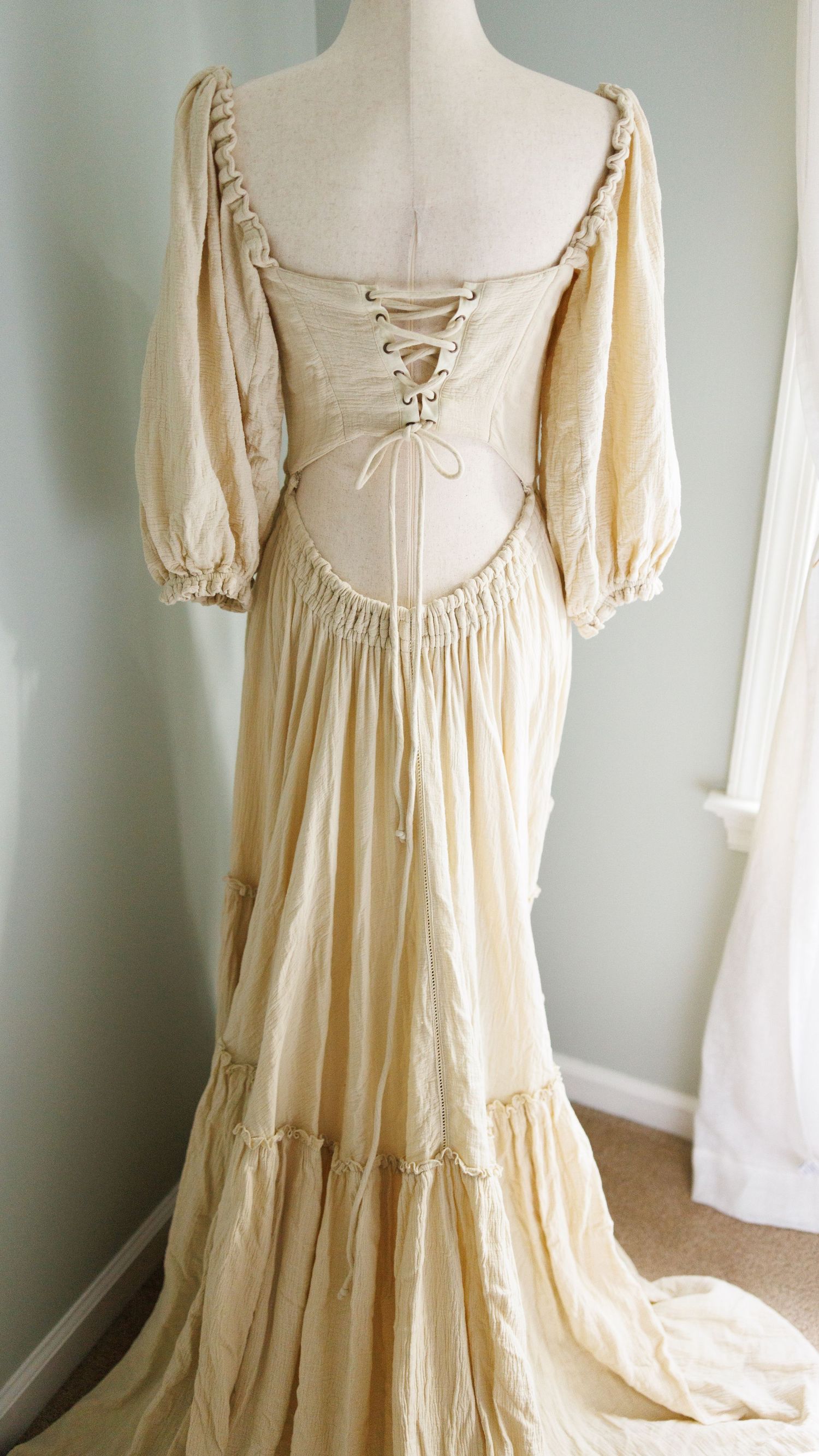 Vintage cream-colored peasant dress with puff sleeves and corset back lacing displayed on mannequin from multiple angles.