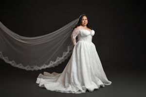 A flowing white wedding dress with lace details and long train photographed in dramatic lighting against a dark background.