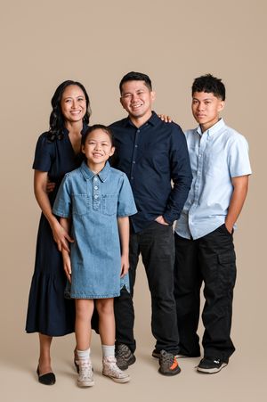 Family of four posing together in coordinating blue outfits against a warm beige studio background.