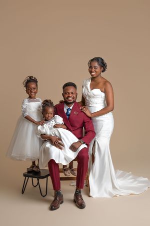 A joyful family in wedding attire poses together, with the groom in burgundy and bride in white gown.