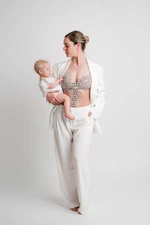Elegant maternity photography session featuring soft white clothing and delicate lace details against a light studio backdrop.