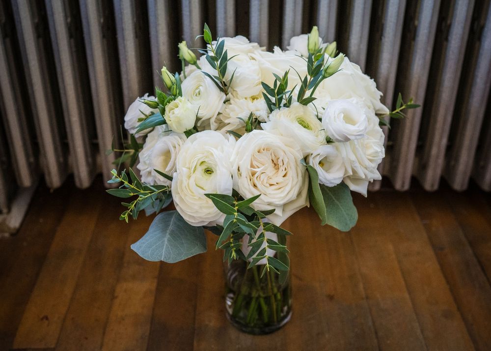 White roses and floral arrangements in glass vases displayed on a wooden floor against a striped wall.