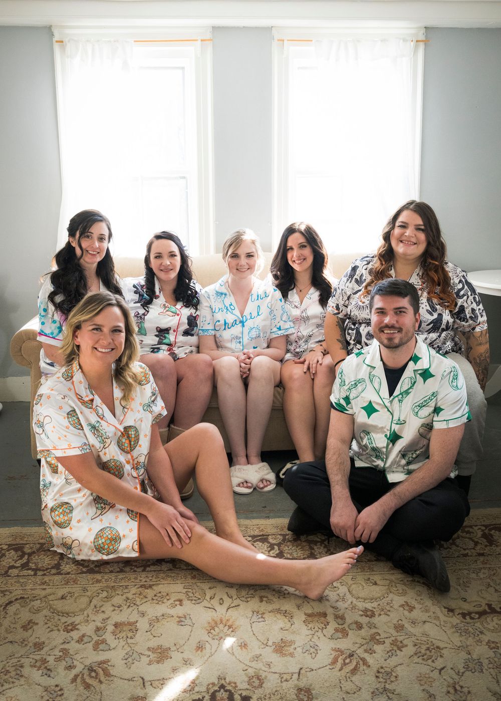Wedding party in floral robes relaxing together on carpeted floor in sunlit room.
