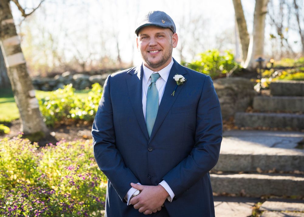 Couple in formal wedding attire poses outdoors in a garden setting with natural sunlight.