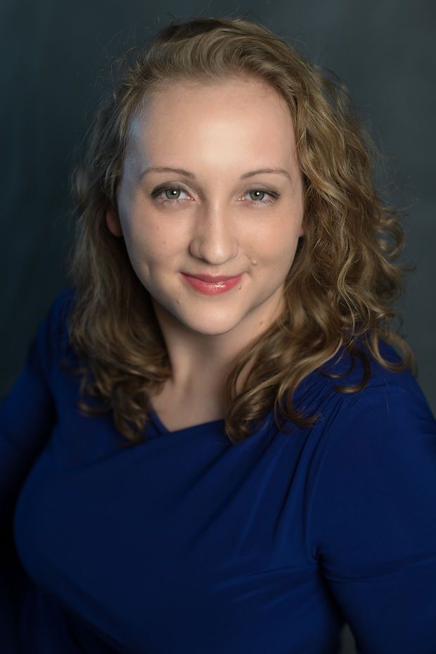 Smiling young woman with curly blonde hair wearing a blue top in a professional headshot.