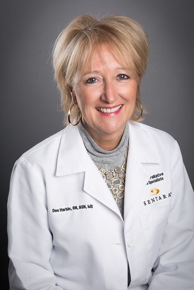 Medical person smiles in a white Sentara medical coat over a gray turtleneck in a professional headshot.