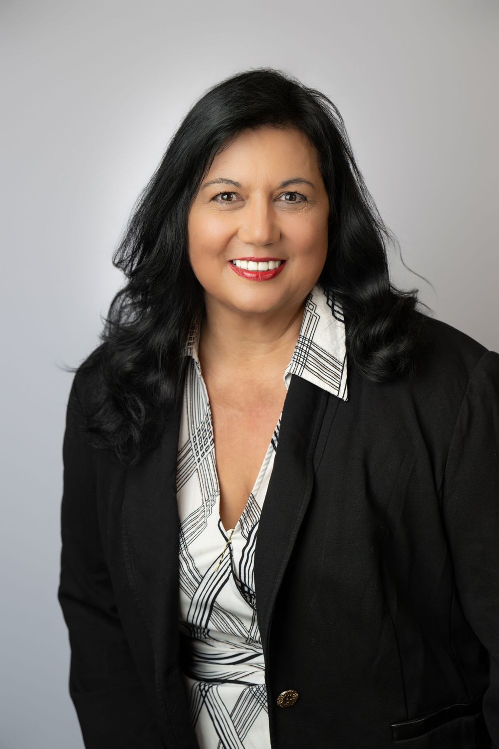 Professional headshot smiling woman dark hair in a black blazer and blouse against a grey background. Best photographer Williamsburg, VA