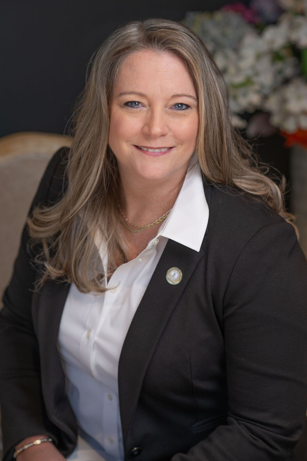 Professional woman in black blazer and white shirt smiling confidently in a formal portrait setting. Best photographer Williamsburg VA