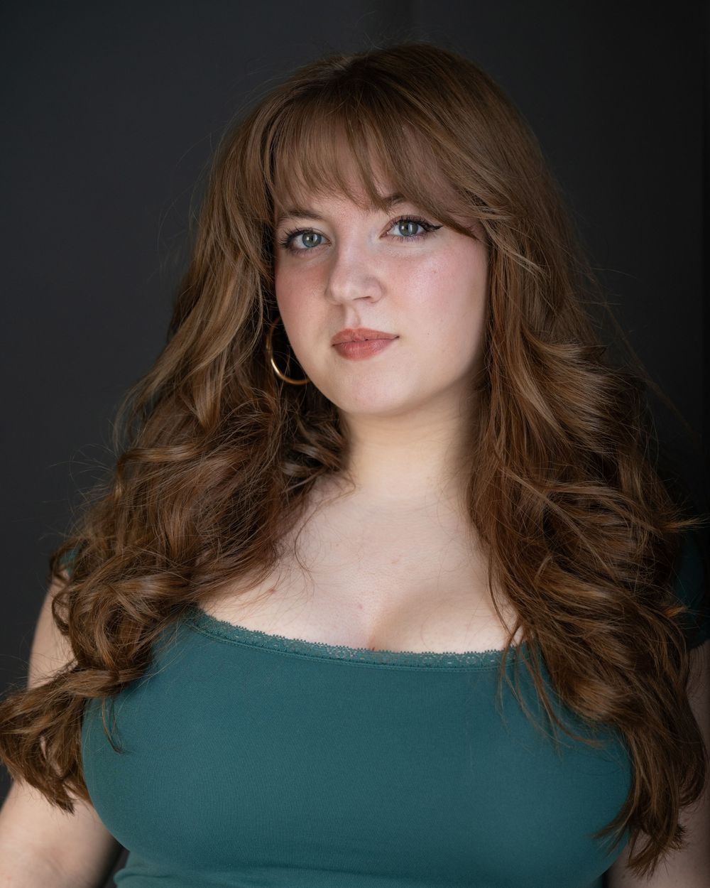 Young woman with long auburn wavy hair and bangs wearing a teal top, posing for a professional headshot. Best photographer Williamsburg VA