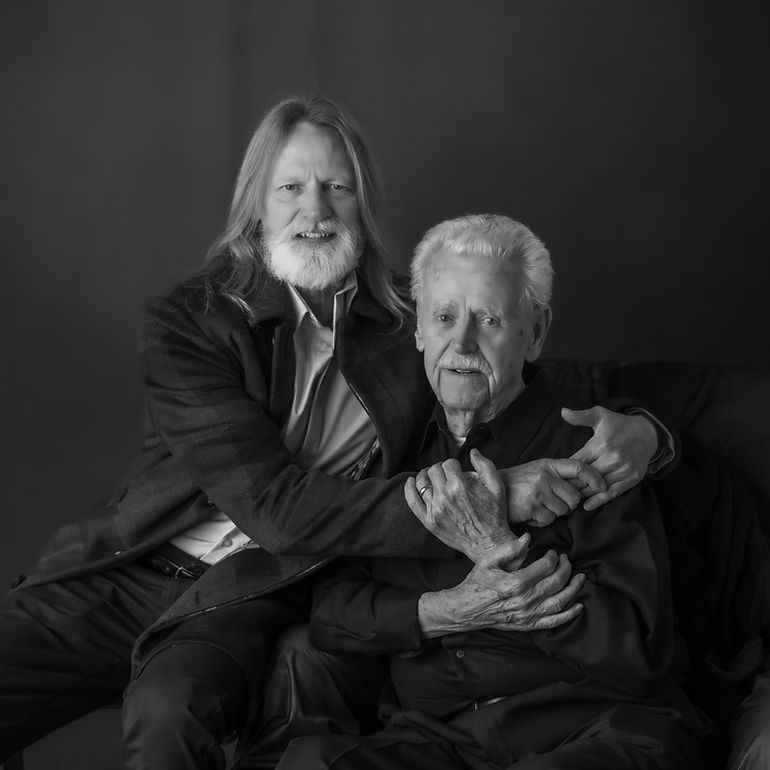 Black and white portrait of two older men posing together affectionately in a studio setting.