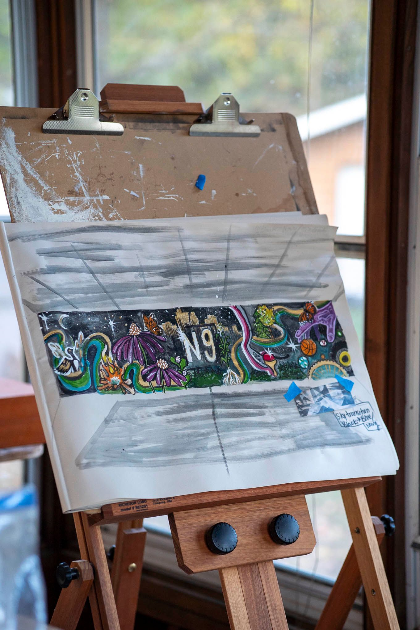 Three wooden easels displaying panoramic artwork with graffiti-style designs against a blurred background.