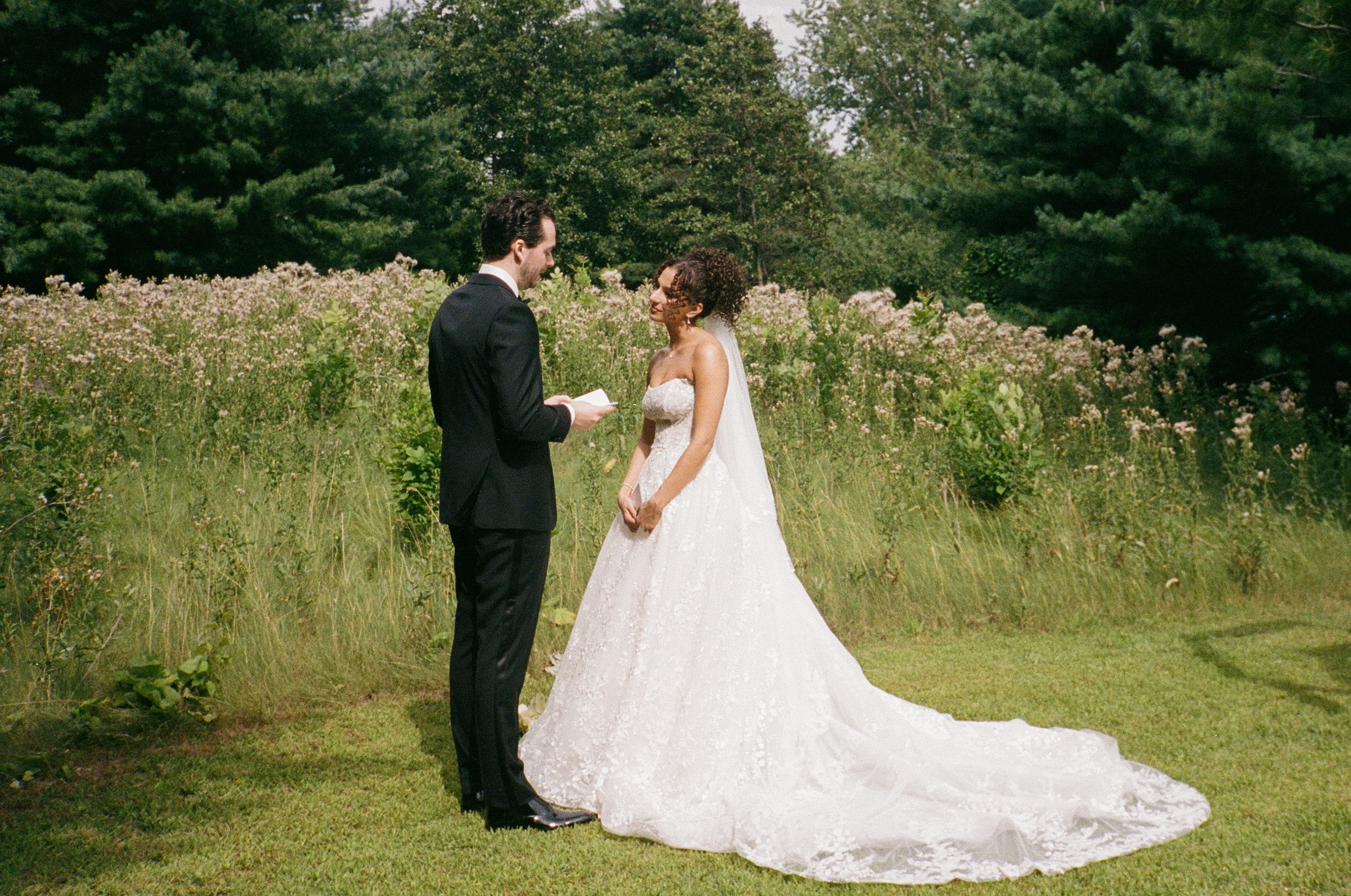 A romantic outdoor wedding photoshoot featuring a couple in formal attire surrounded by lush greenery and wildflowers.