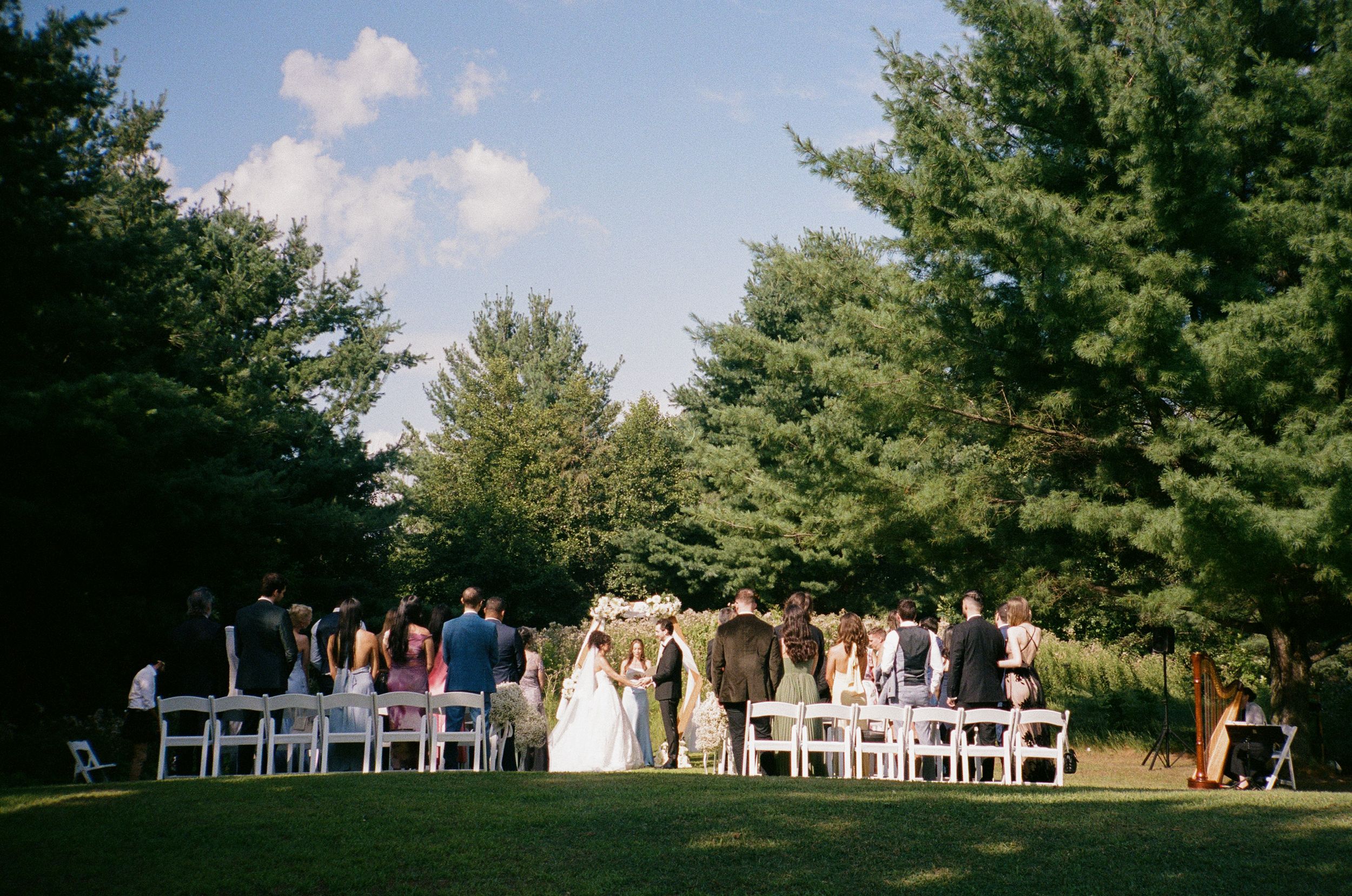 A sequence of outdoor wedding ceremony photos showing white chairs arranged in rows under tall pine trees.