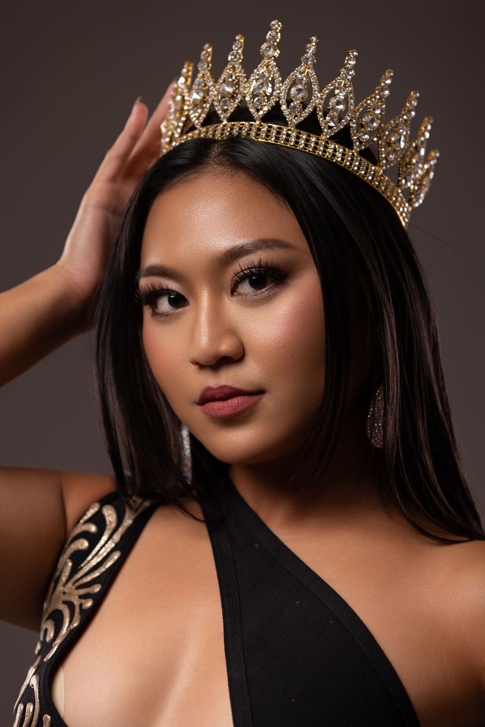 Dramatic studio portrait wearing gold crown and black formal dress.