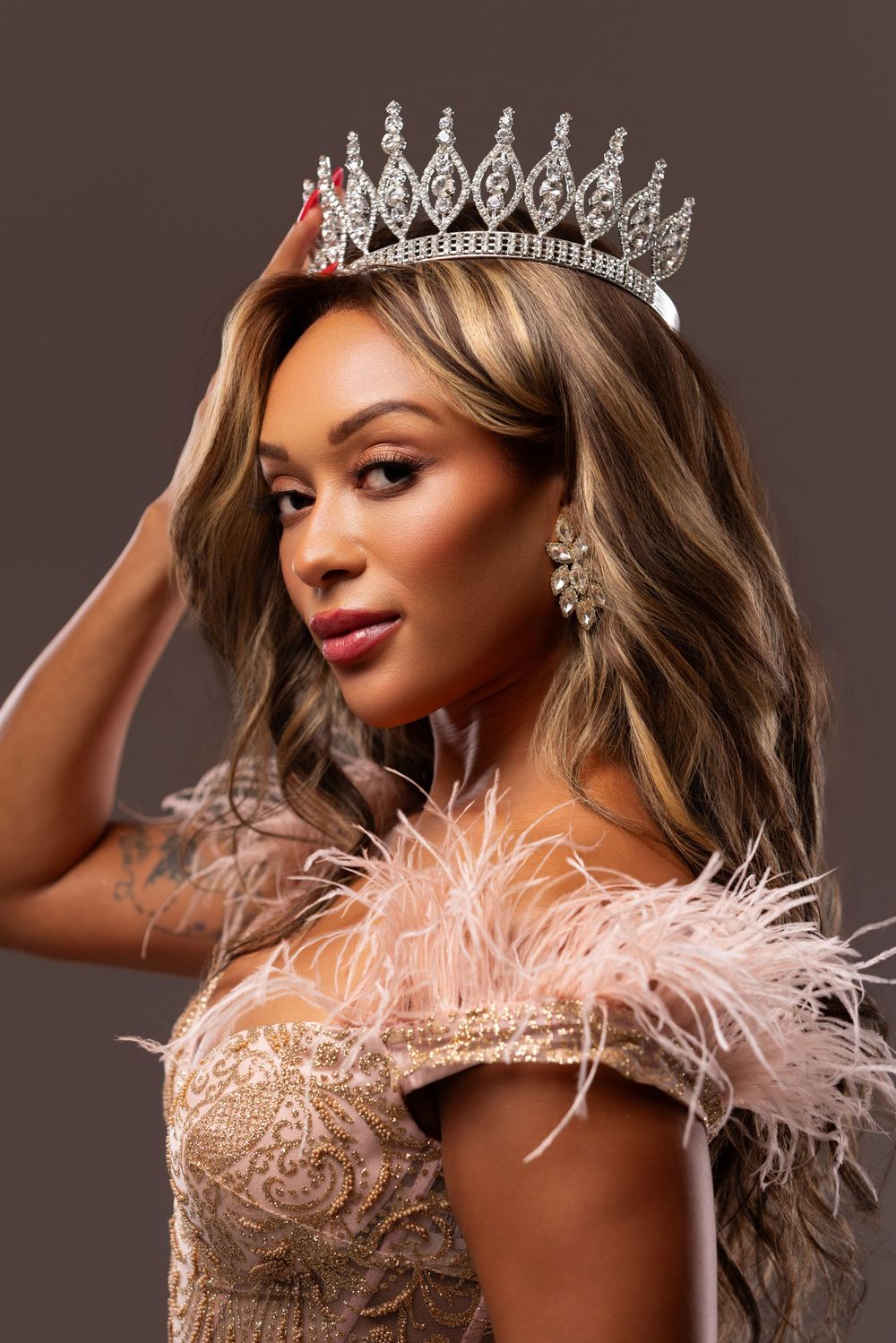 Glamorous portrait with sparkling crown and feathered pink dress.
