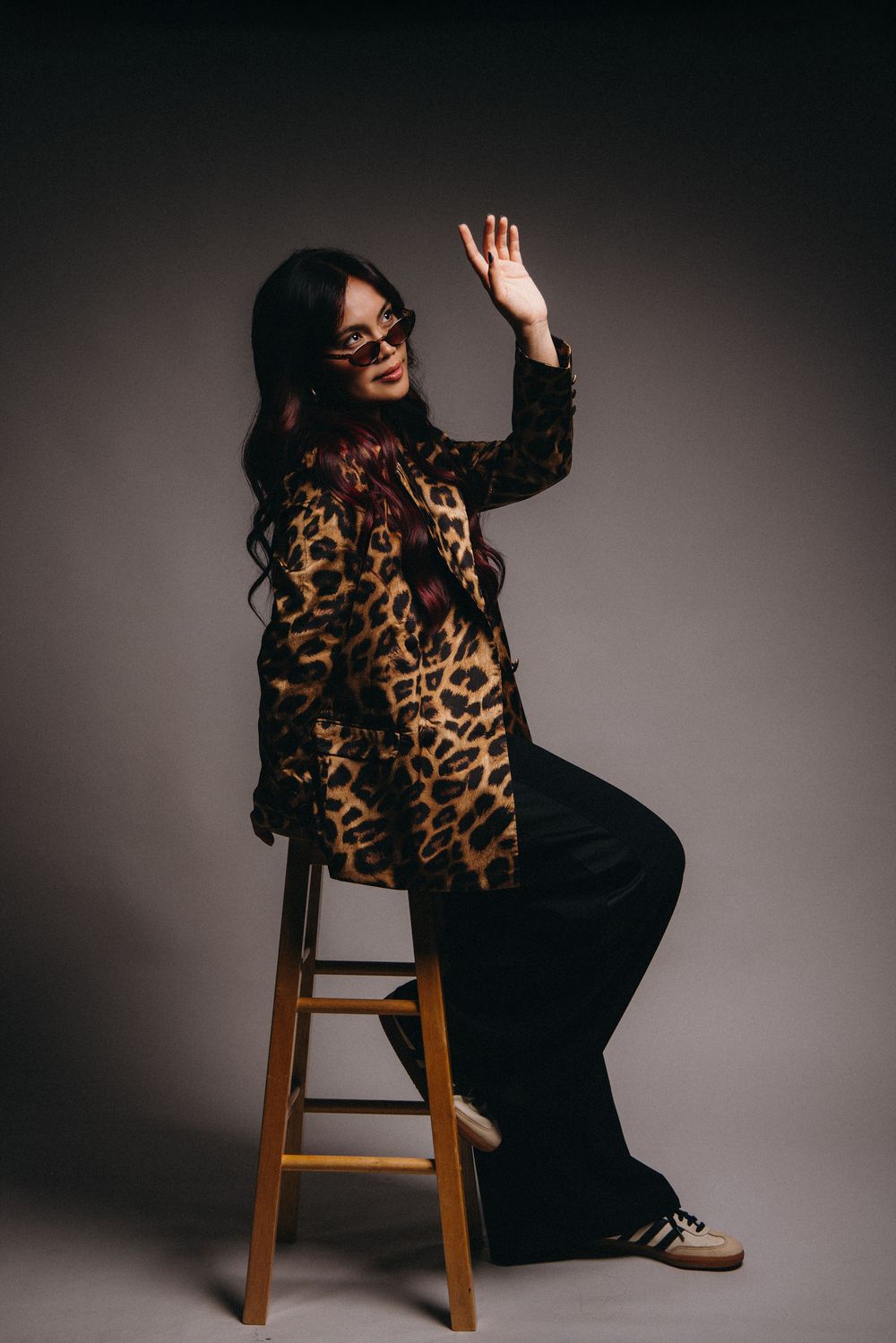 Fashion portrait with leopard print top and black outfit on wooden stool.