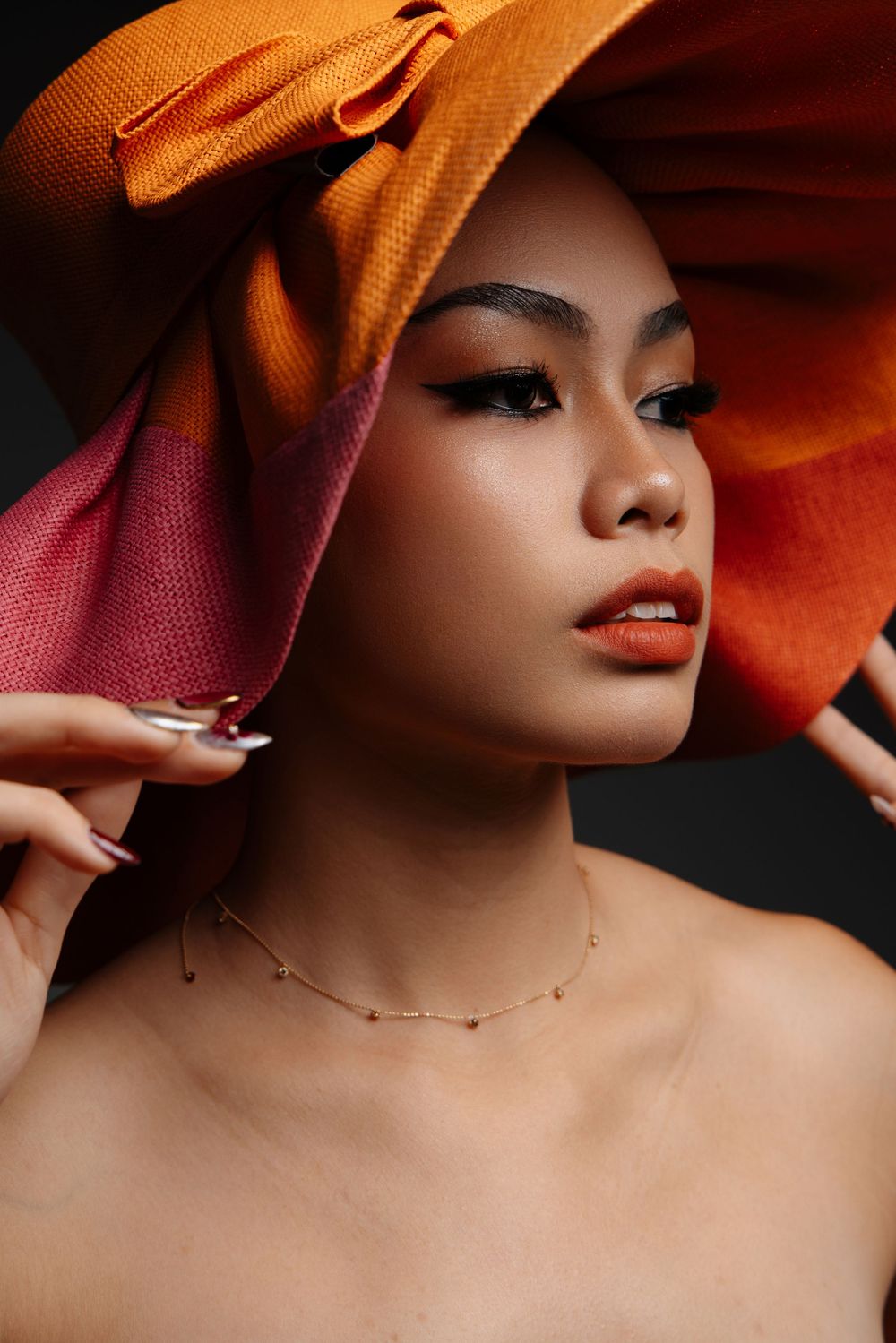Close-up beauty shot featuring orange hat and glamorous makeup.
