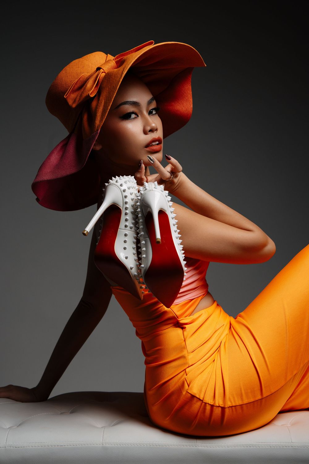 Fashion photo of model in orange dress and dramatic hat posing on floor.