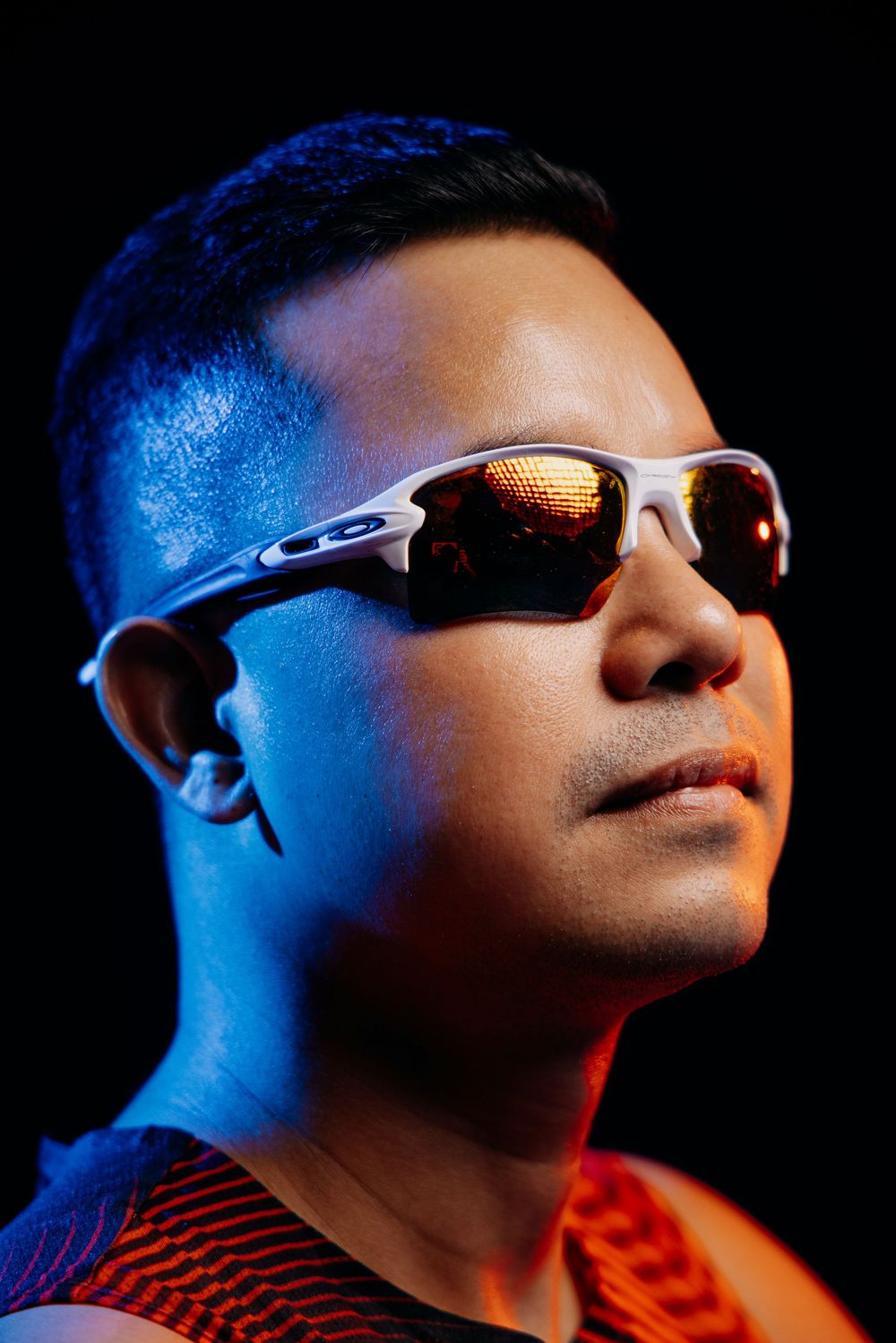 Dramatic profile portrait with blue lighting and sports sunglasses.