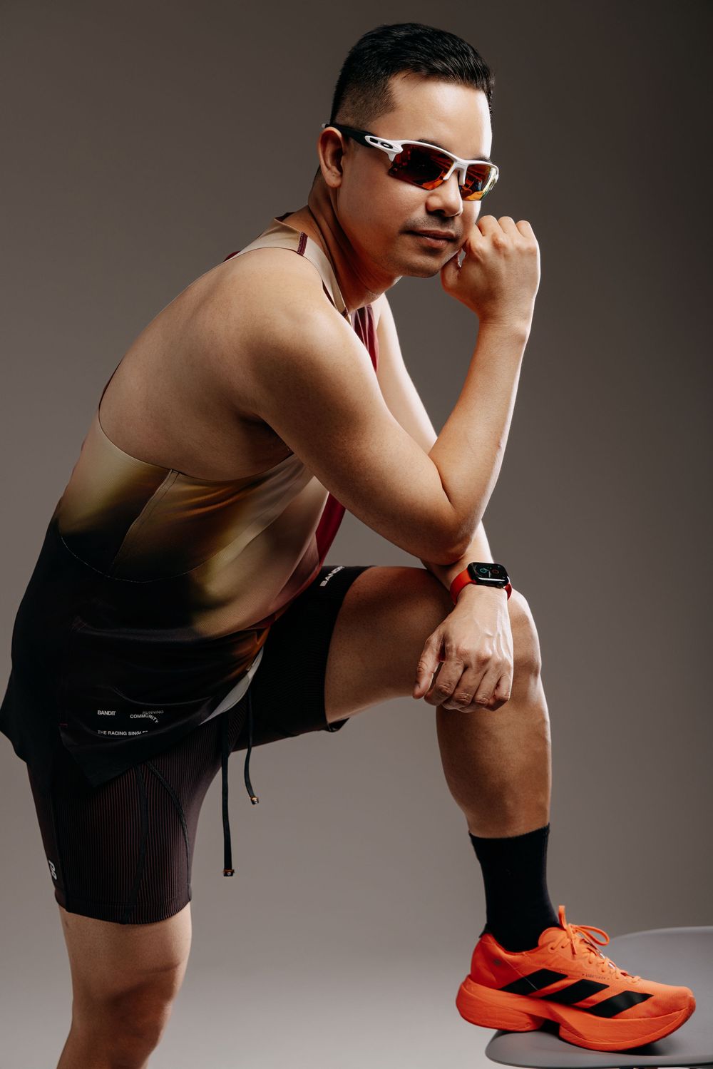 Athletic figure in black shorts and orange shoes poses against studio backdrop.