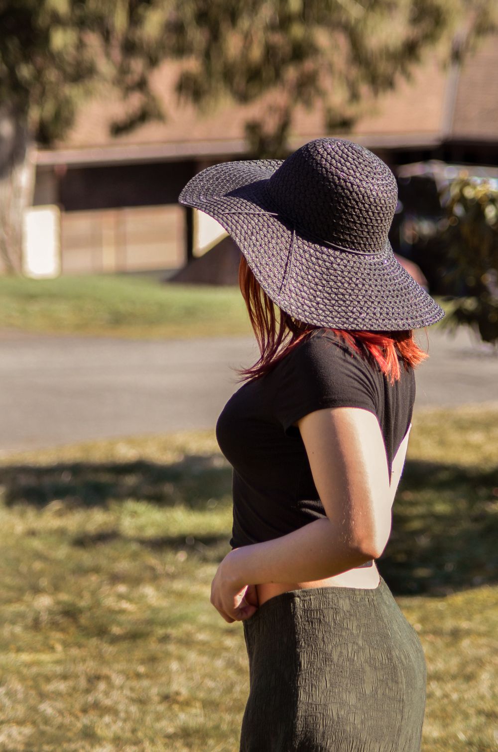A person in a wide-brimmed sun hat and black top stands in a sunlit garden on a warm afternoon.